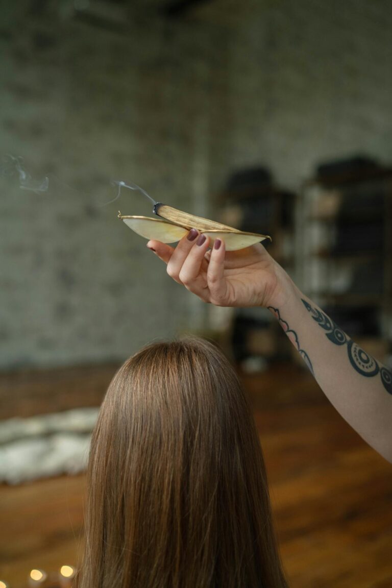 A woman performing a cleansing ritual using sage indoors, creating a serene atmosphere.