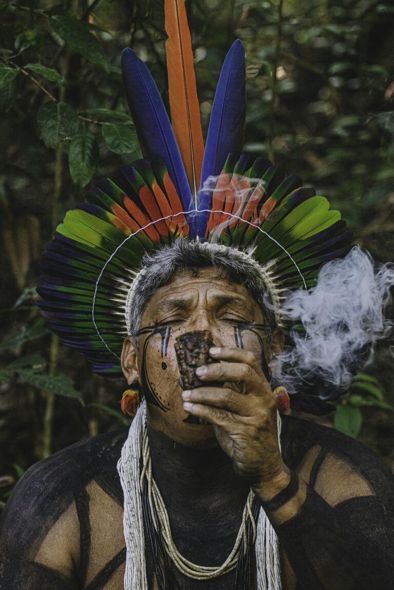 Portrait of an indigenous man with traditional attire and smoke in a Brazilian forest.